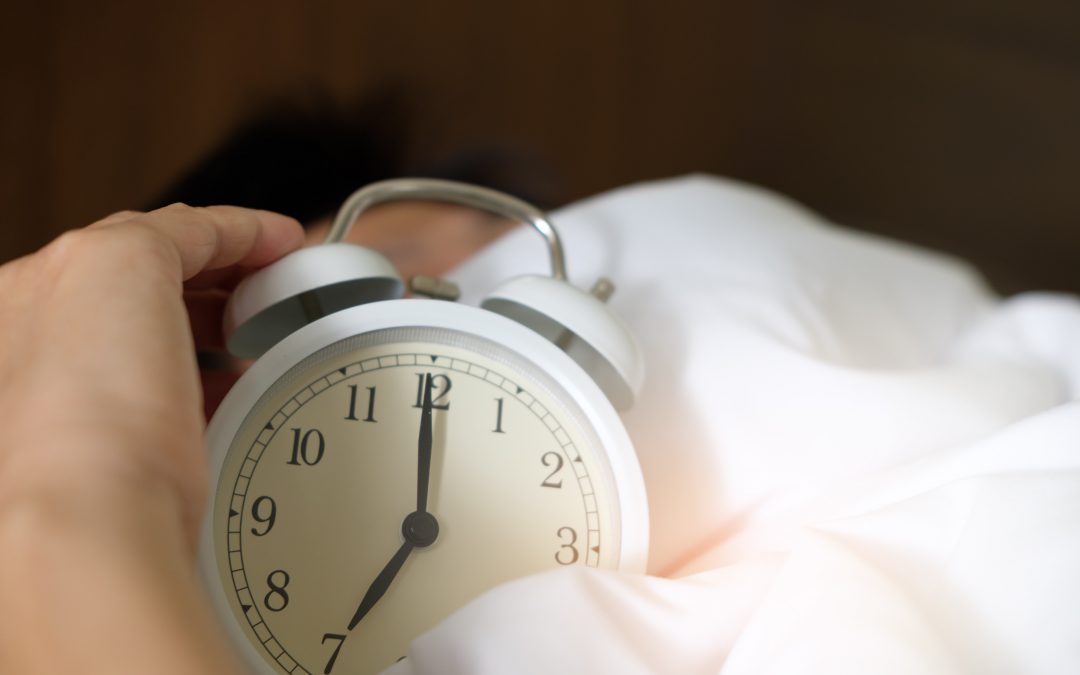 man holds clock in bed to get more sleep